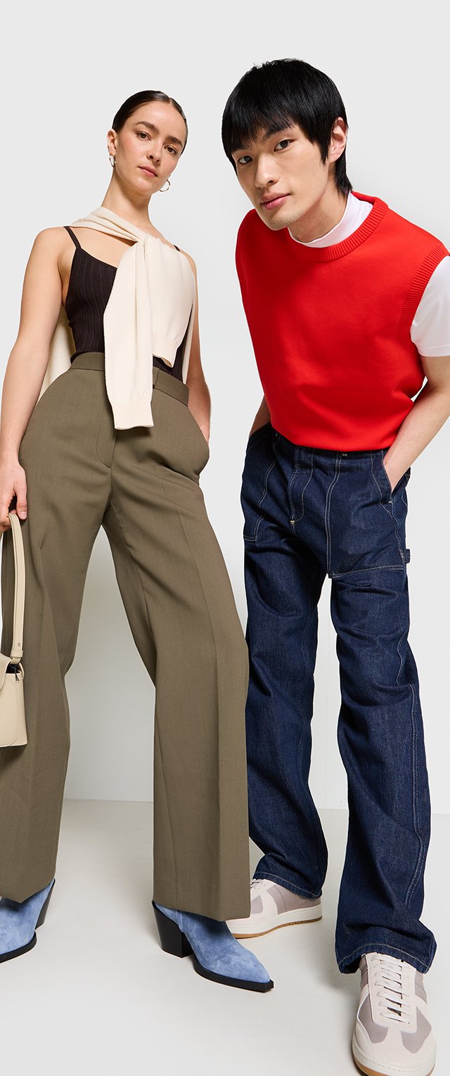 Deux mannequins se tiennent côte à côte. L'un porte un haut beige, un pantalon large olive et des bottes à talons bleues. L'autre porte un pull rouge par-dessus une chemise blanche et un pantalon en denim foncé.