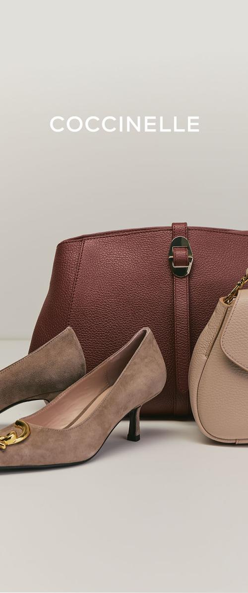 Twee beige suède hakken met gouden accenten geplaatst voor een grote donkerbruine leren handtas en een kleinere beige leren handtas.