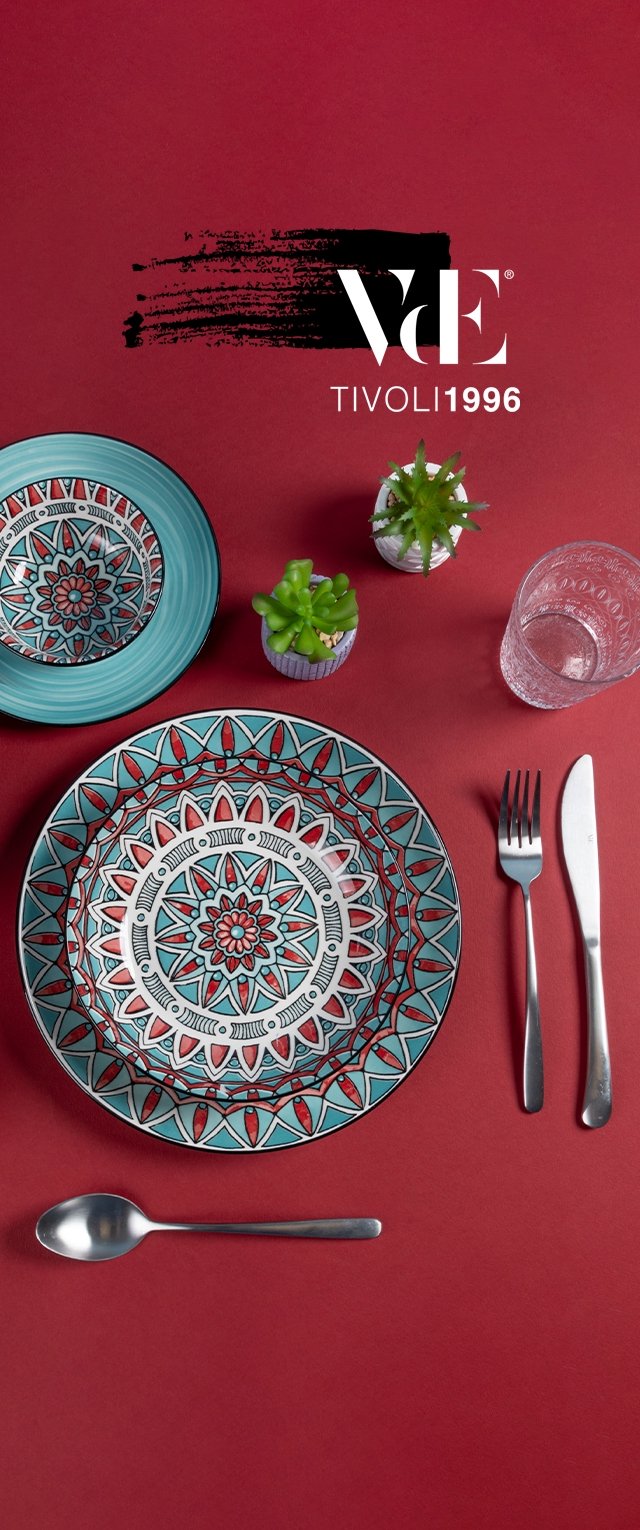 Keramikteller mit aufwendigen türkisfarbenen und roten geometrischen Mustern, begleitet von silbernem Besteck und einem Glas auf einer roten Oberfläche.