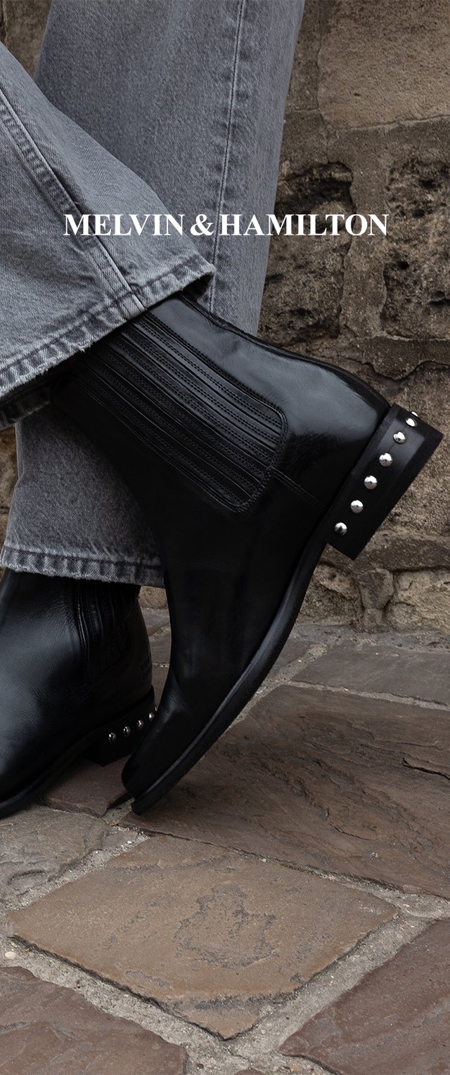 Schwarzer Lederknöchelstiefel mit geripptem elastischem Einsatz an der Seite, runder Spitze und dekorativen silbernen Nieten an der Ferse. Getragen zu grauer Denim.