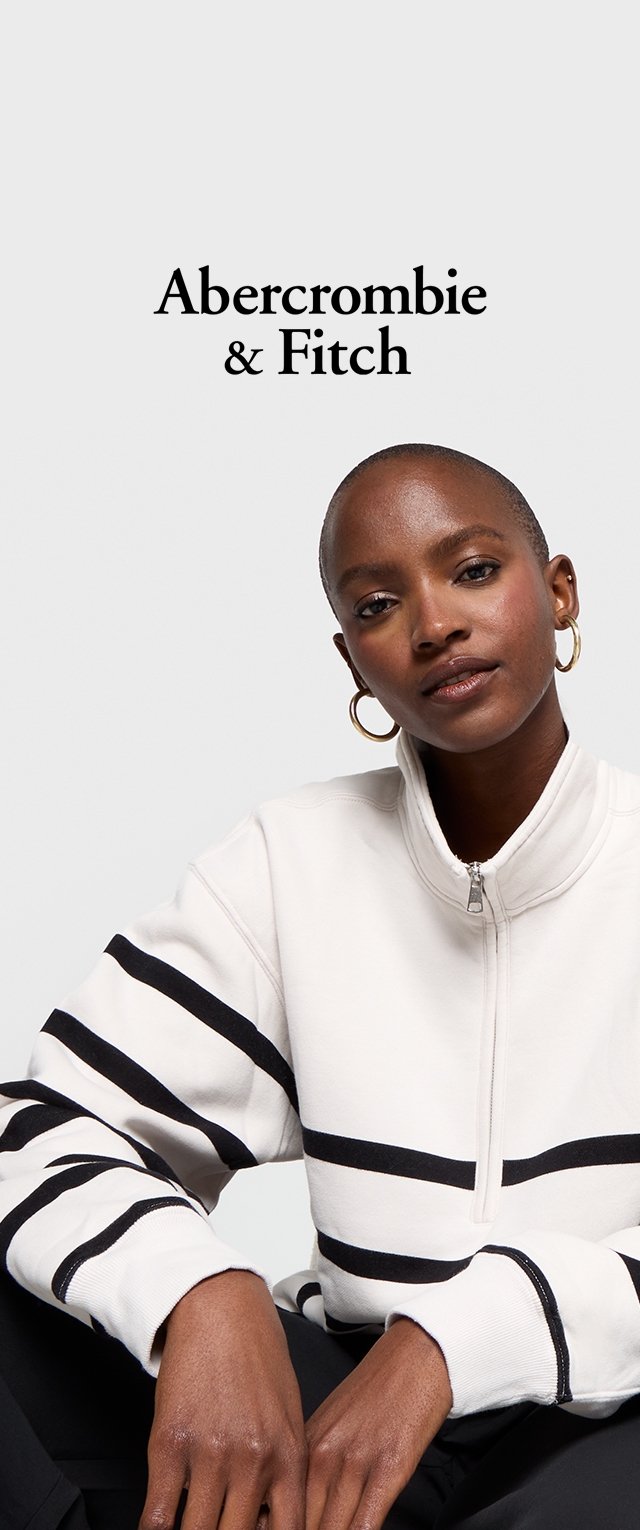 Witte zip-up sweatshirt met zwarte horizontale strepen, voorzien van een hoge kraag en elastische manchetten. Model draagt gouden oorbellen.