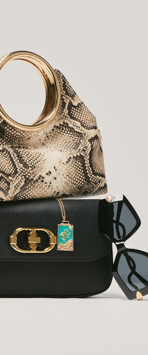 Sac texturé à imprimé serpent avec poignée dorée, superposé sur un sac en cuir noir orné de ferrures dorées et d'une étiquette turquoise, à côté de lunettes de soleil noires.