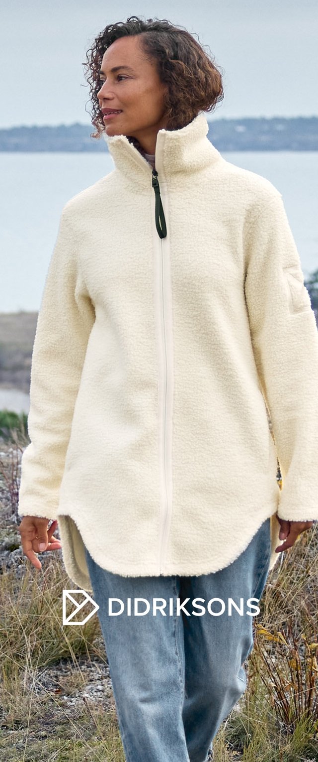 Kremowa polarowa kurtka z wysokim kołnierzem, pełnym zamkiem z przodu i zakrzywionym dołem. Noszona na niebieskich dżinsach, w plenerze.