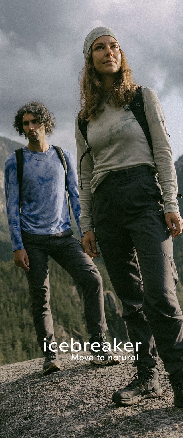 Dos excursionistas al aire libre llevan camisetas de secado rápido, una de color azul atigrado y otra gris claro. Ambos llevan pantalones oscuros y calzado resistente en un terreno rocoso.