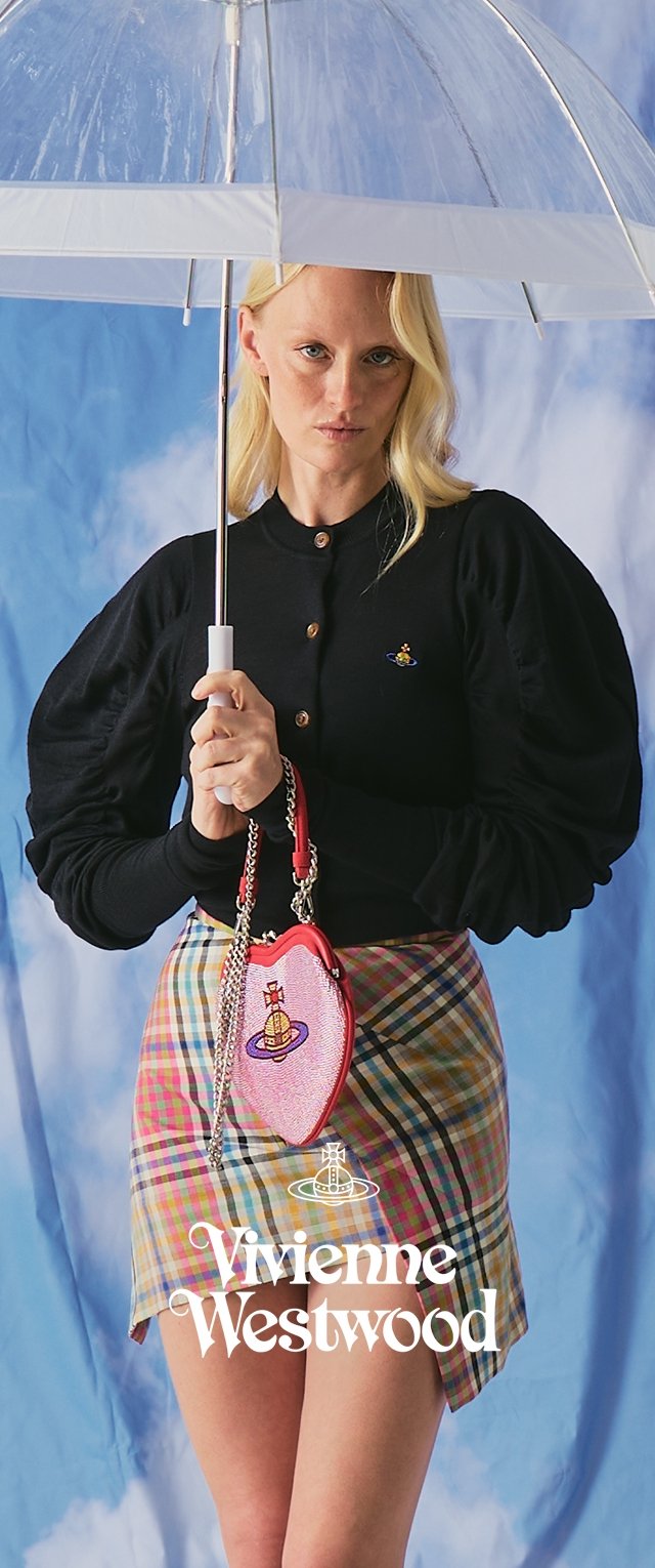 Femme tenant un parapluie transparent, portant un haut noir à manches bouffantes, une jupe à carreaux, et tenant un sac rouge en forme de cœur avec le logo Vivienne Westwood.