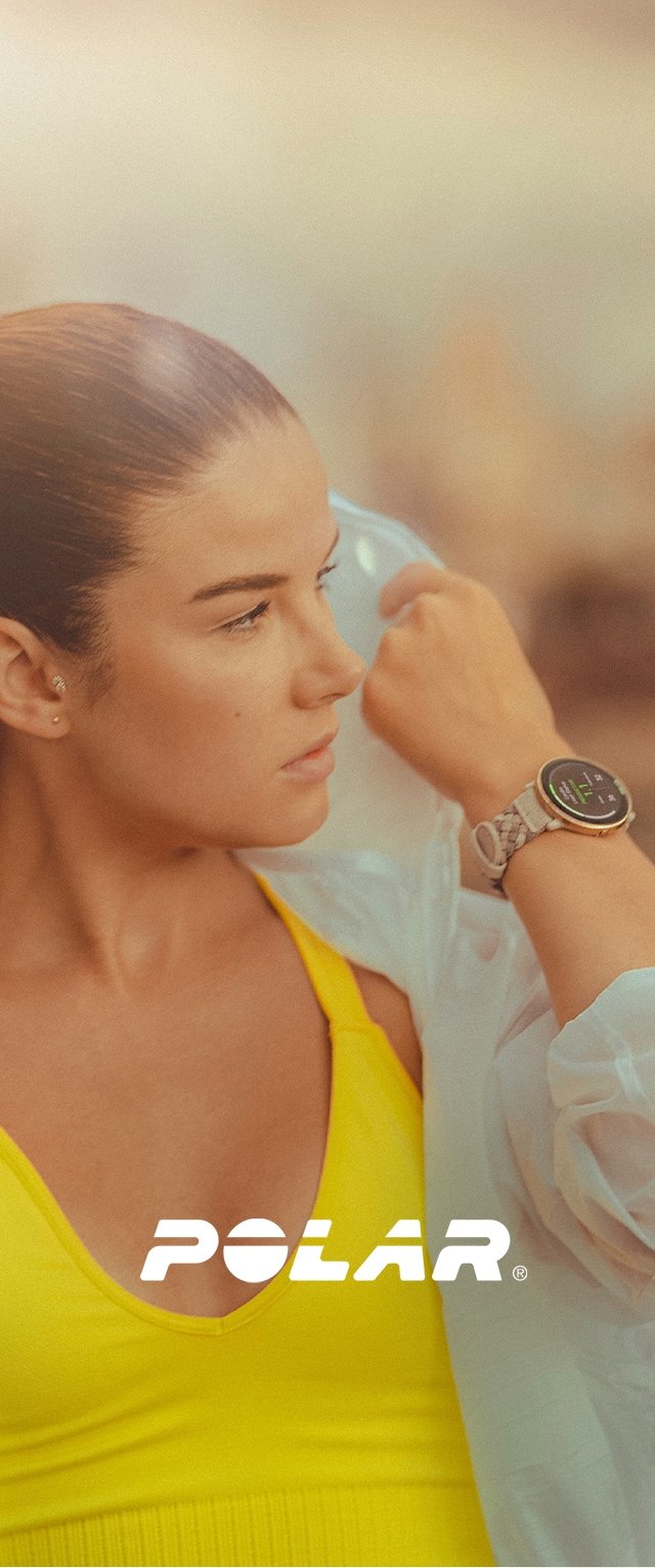 Silberner Smartwatch mit rundem Zifferblatt, das grüne Werte anzeigt, am Handgelenk getragen. Der Hintergrund weist warme Farbtöne auf. Produktlogo sichtbar.