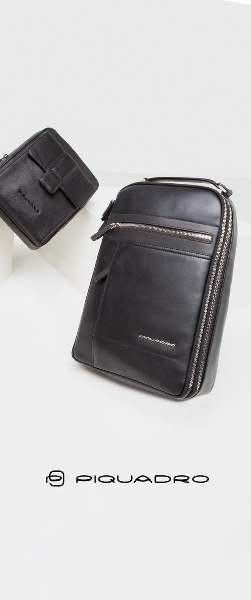 Sac à dos en cuir noir avec une texture lisse, doté de fermetures éclair et d'une poche avant. Un petit étui en cuir noir l'accompagne, les deux étant minimalistes.