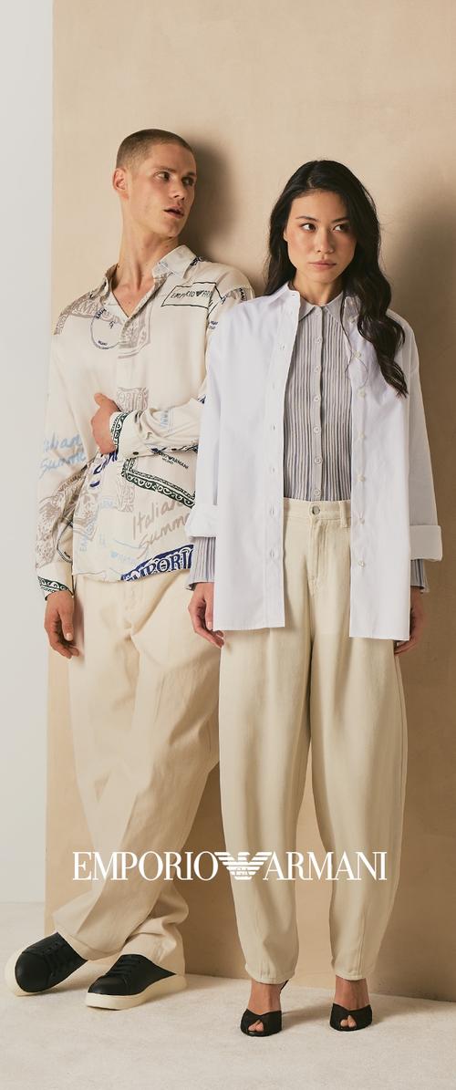 Hombre con camisa abotonada de estampado y pantalones crema con zapatillas negras, mujer con chaqueta blanca abierta, camisa a rayas, pantalones crema y tacones negros.