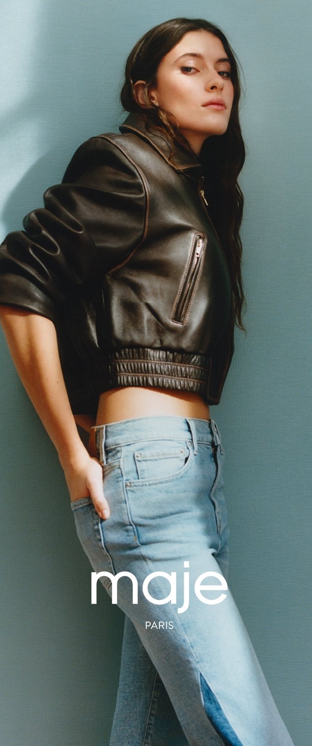 Chaqueta bomber de cuero negro con puños de canalé, combinada con jeans de cintura alta de color azul claro con una abertura lateral. El fondo es de un azul claro texturizado.