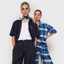 Dva modelky stojí vedle sebe. Jedna má na sobě námořnickou košili a široké kalhoty; druhá má modrý kombinézu s tie-dye vzorem. Obě mají minimum doplňků.