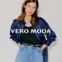 Mladá žena oblečená v tmavě modré saténové košili přes černé tílko, světle modré džíny s vysokým pasem a černé špičaté podpatky s průchodkami.