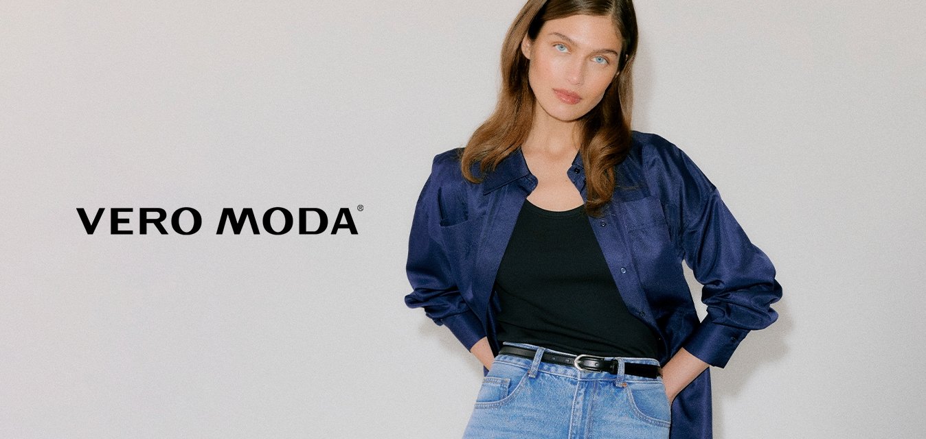 Mladá žena oblečená v tmavě modré saténové košili přes černé tílko, světle modré džíny s vysokým pasem a černé špičaté podpatky s průchodkami.