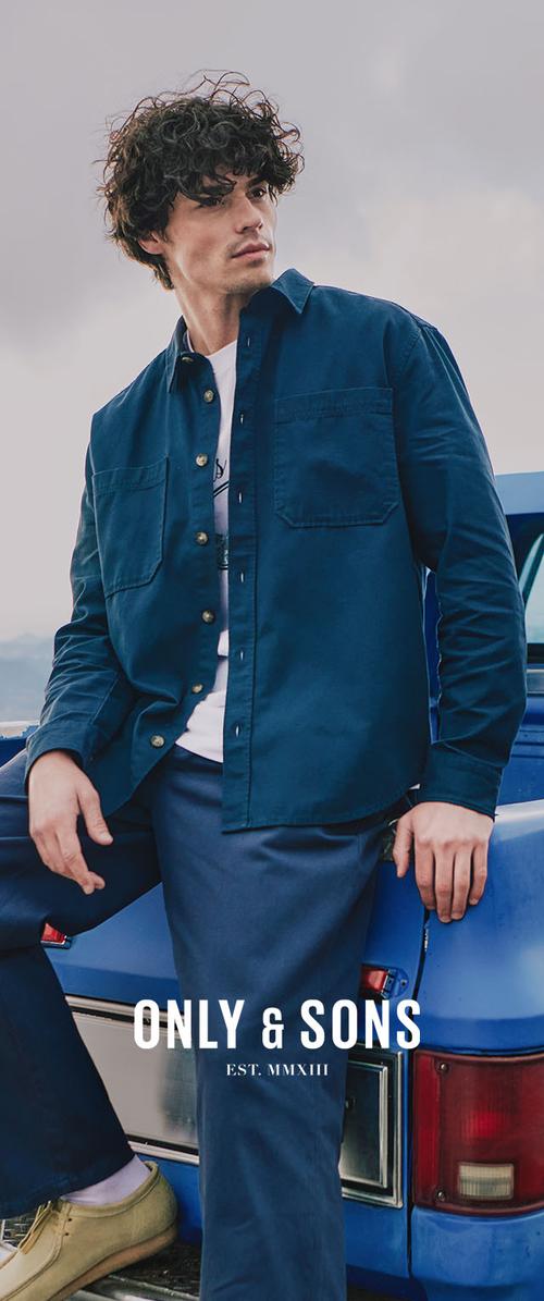 Homme en chemise et pantalon bleus assis sur une voiture bleue, regardant sur le côté. Texte : "ONLY & SONS EST. MMXIII.". Scène de mode décontractée en extérieur.