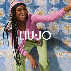 Růžový žebrovaný kardigan, světle růžové tričko a zelené kalhoty s hladkou texturou. Pozadí tvoří modré dlaždice s květinovými vzory v žluté a bílé barvě.