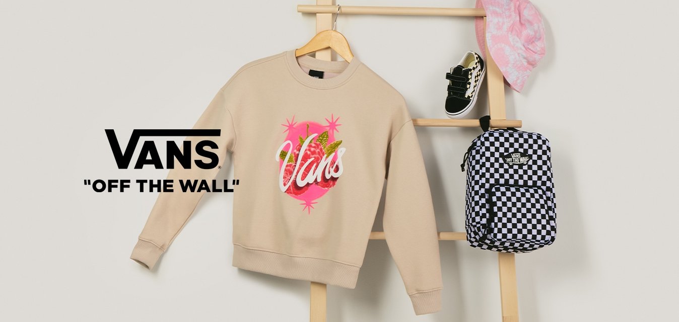 Béžová mikina Vans, černo-bílý kostičkovaný batoh, růžový klobouk s potiskem a černé dětské tenisky vystavené na dřevěném žebříku.