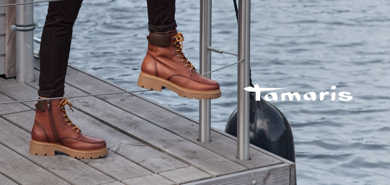 Hnědý nepromokavý kabát s límcem, krémový svetr, černé kalhoty a hnědé kotníkové boty s tkaničkami a silnou podrážkou. Dřevěné a kovové prostředí.