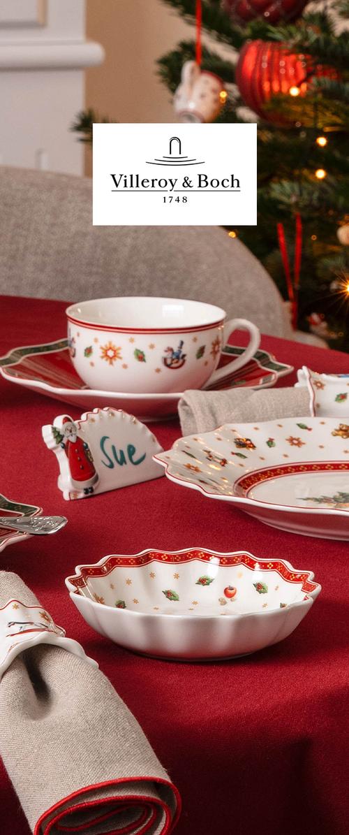 Veselă de porțelan cu tematică de Crăciun cu ilex și modele festive pe o față de masă roșie, inclusiv un cartonaș cu nume inscripționat "Sue."