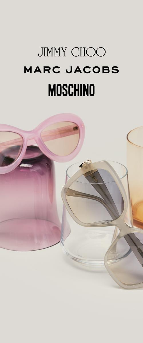 Roze cat-eye zonnebril op een paarse glas, beige oversized zonnebril rustend op een heldere glas, merknamen erboven.