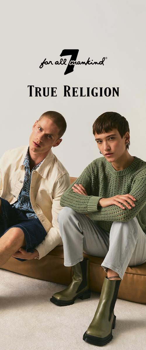 Two male models seated; one wears beige jacket and shorts, the other green knit sweater, light pants, and green boots; True Religion logo above.
