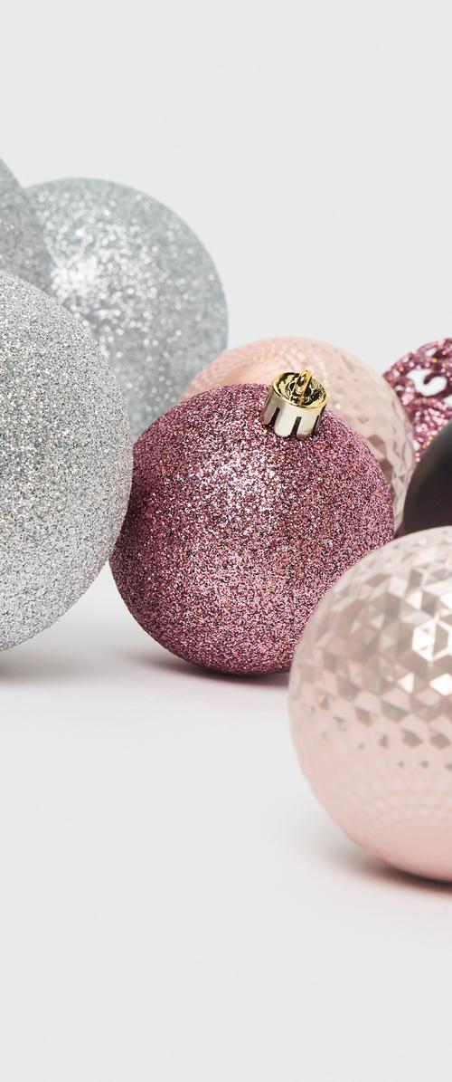 Ornements de Noël variés en rose, argent et noir. Les caractéristiques varient : surfaces brillantes, pailletées et texturées en formes rondes et facettées.