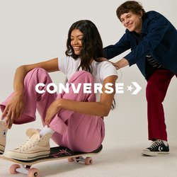 Mladá žena v růžových kalhotách sedí na skateboardu, zatímco ji zezadu tlačí usmívající se muž v bílé studiové místnosti.