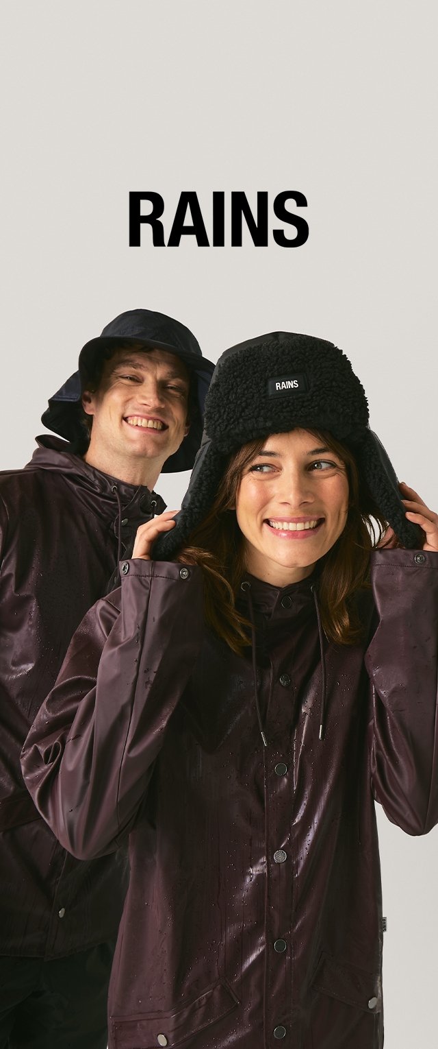 Dos personas llevan chaquetas impermeables de color burdeos oscuro con acabado brillante y botones. Una lleva un gorro negro con orejeras peludas.