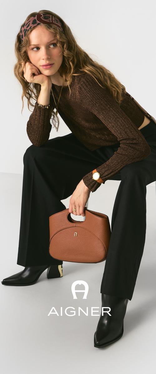 Sac à main en cuir marron avec une forme structurée et une poignée découpée, associé à des bottes noires à talons pointus et un haut noir à manches longues texturé.