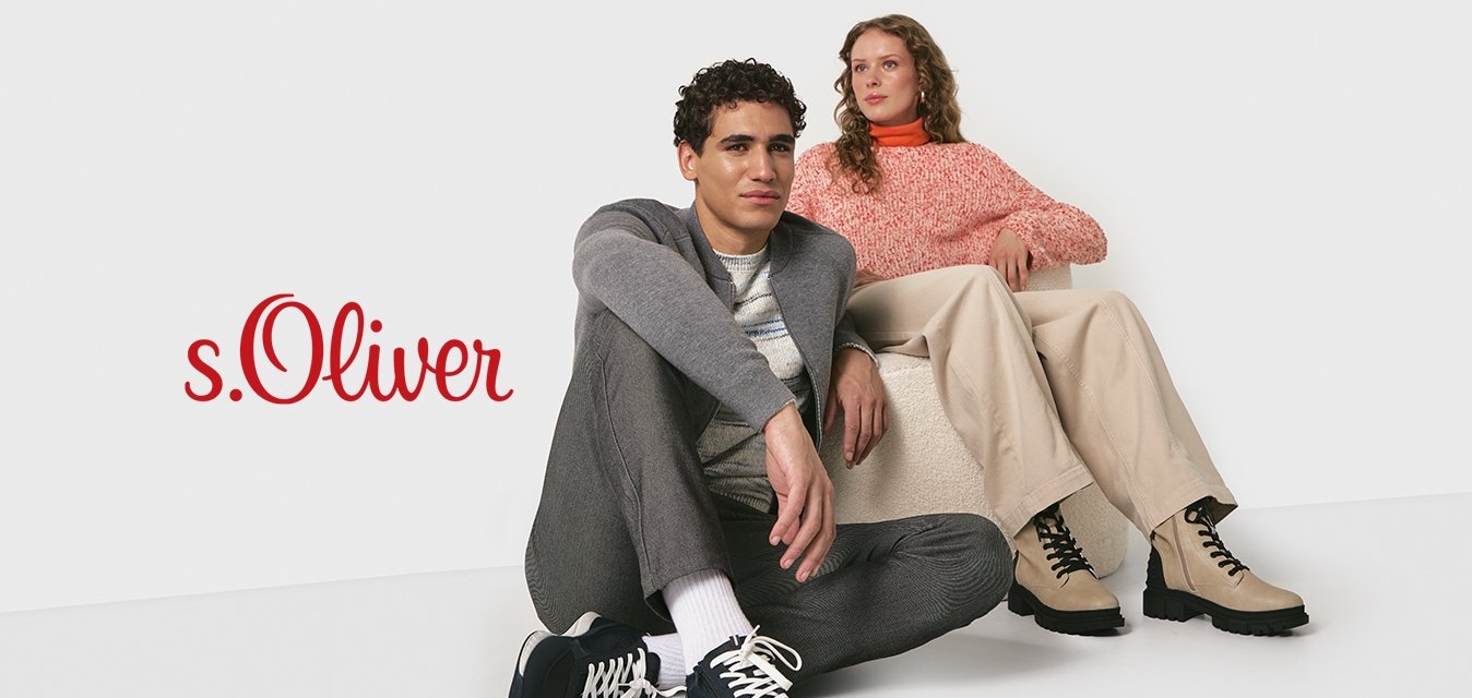 Dva mladí dospělí v neformálním podzimním oblečení; jeden sedí na podlaze v teniskách, druhý na nízkém sedadle v béžových botách na bílém pozadí.