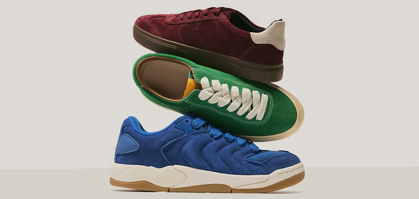 Tři naskládané semišové sneakers v modré, zelené s bílými tkaničkami a burgundské s béžovým detailním podpatkem na neutrálním pozadí.