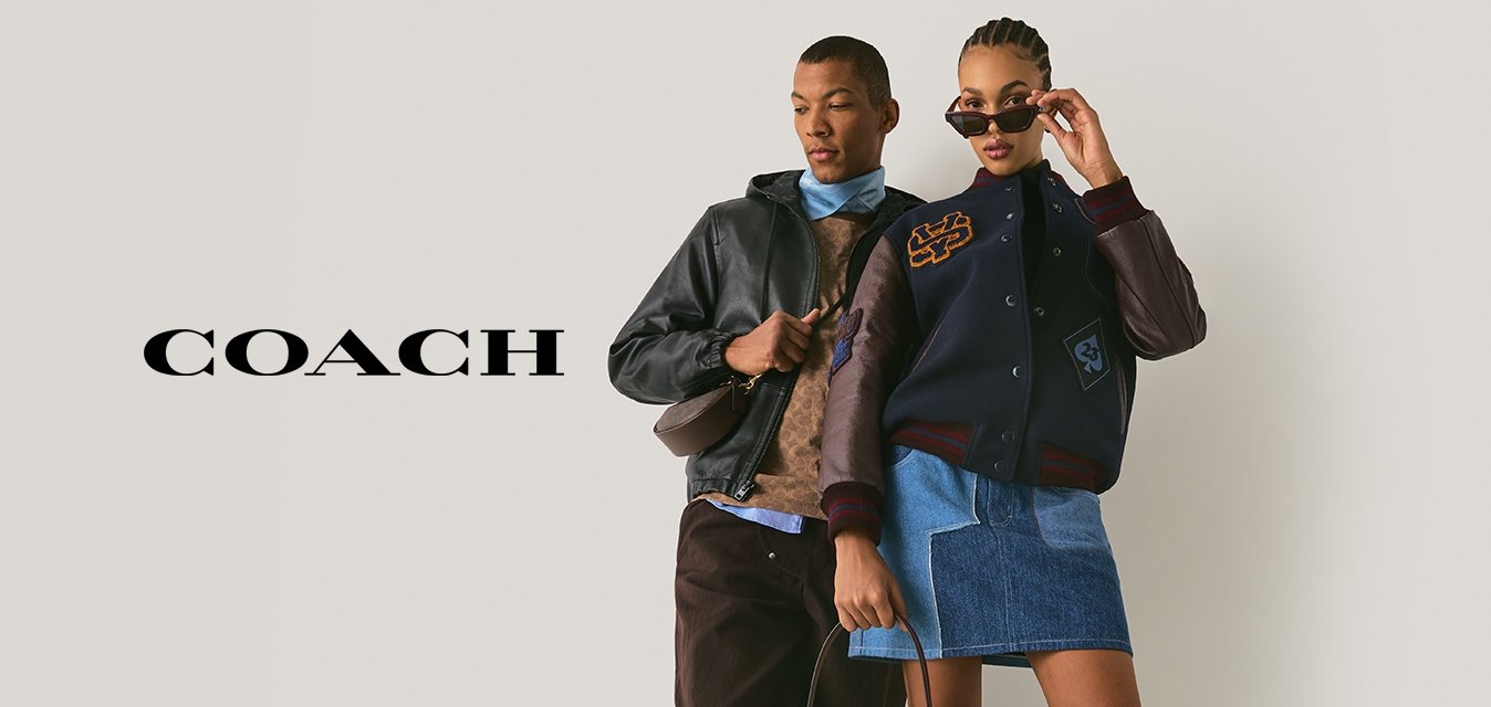 Dva modelky pózují před obyčejnou zdí; jedna v kožené bundě, hnědých kalhotách a teniskách, druhá ve varsity bundě, džínové sukni, botách a slunečních brýlích.