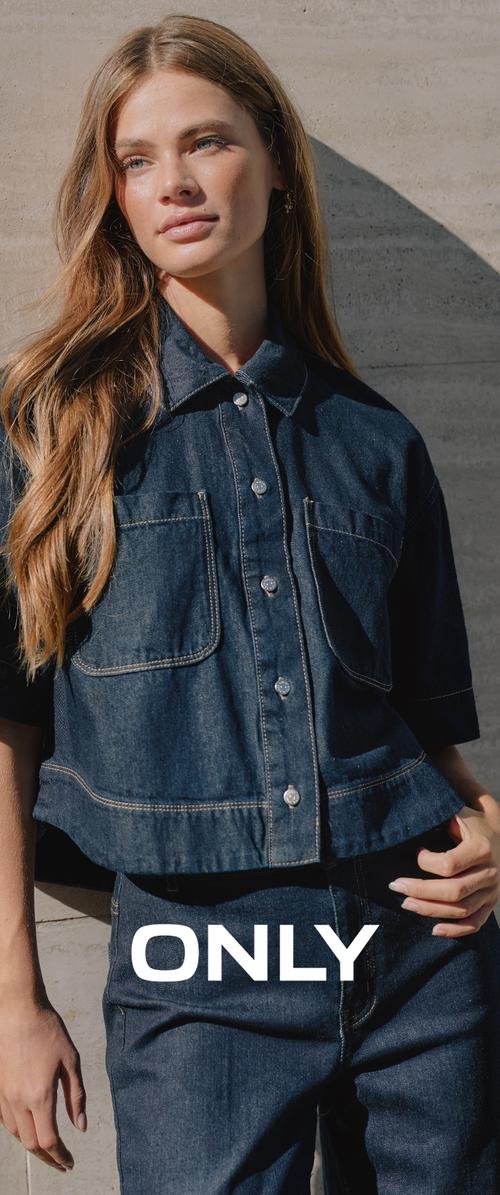 Joven con cabello largo que lleva una chaqueta y jeans de mezclilla oscura, de pie contra una pared de concreto iluminada por el sol con el texto "ONLY" a la altura de la cintura.