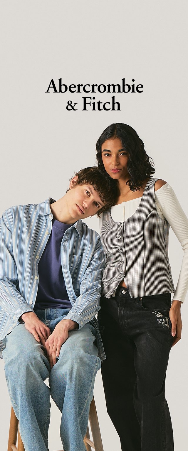 Dvaja mladí dospelí, jeden sediaci v pruhovanom tričku a džínsoch, druhý stojaci v bielom tričku s dlhým rukávom a károvanou vestou, nad nimi logo Abercrombie & Fitch.