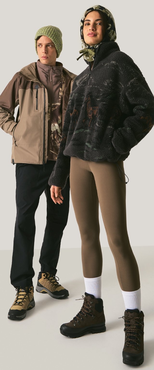 Dos modelos llevan ropa de exterior: una chaqueta marrón con cremallera, una camiseta de forro polar con estampado, mallas marrones y botas. Los accesorios incluyen un gorro verde y un pañuelo para la cabeza.