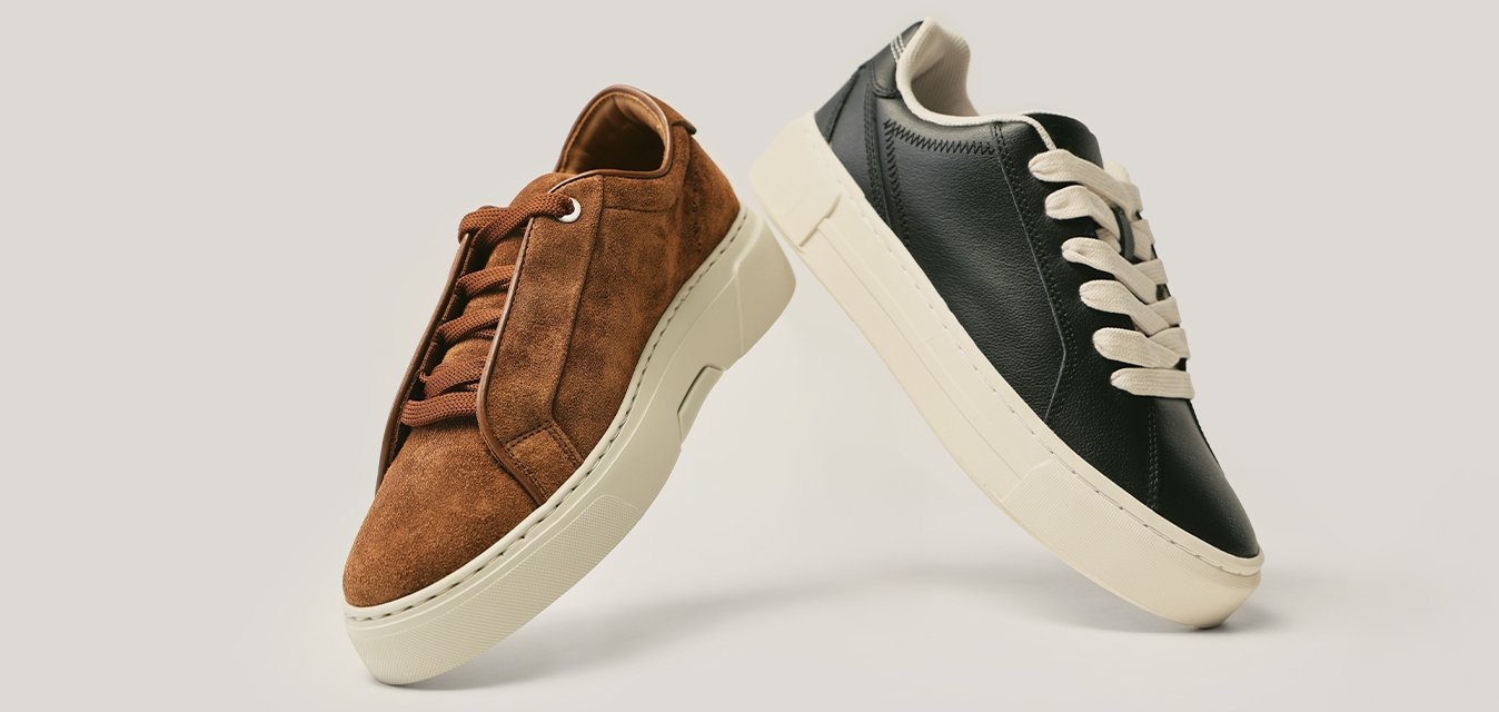 Pár neformálních tenisek s nízkým střihem, jedna z hnědé semiše a druhá z černé kůže, obě s bílými podrážkami a odpovídajícími tkaničkami, vystavené na světlém pozadí.