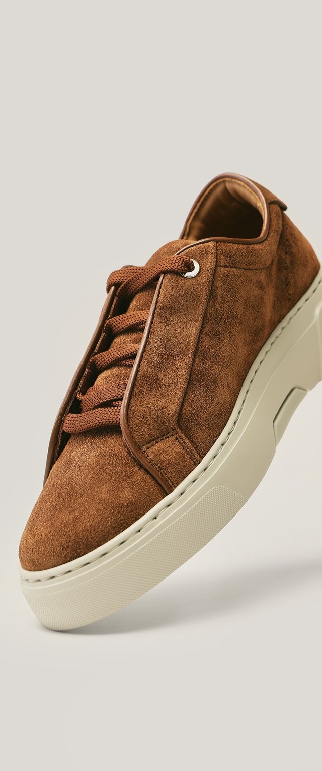 Zapatilla marrón de ante con punta redondeada, parte superior texturizada, cordones planos y una suela gruesa de goma color blanco roto. Cuenta con ojales reforzados.