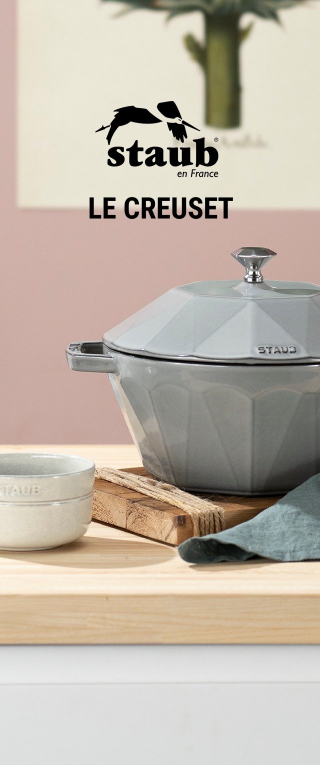 Grijze octagonale gietijzeren cocotte met een glanzende afwerking en een metalen knop op het deksel, vergezeld van een klein rond steengoedkommetje en een groene doek.
