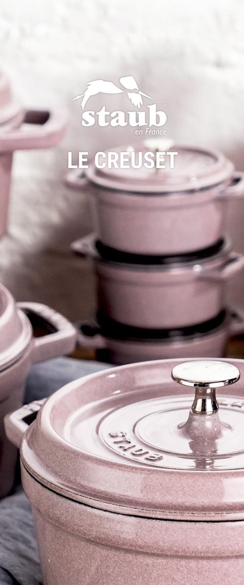 Gestapelte pinke keramische Staub-Kochgeschirre, einschließlich Töpfen mit Deckeln und Metallgriffen, vor einem unscharfen neutralen Hintergrund.