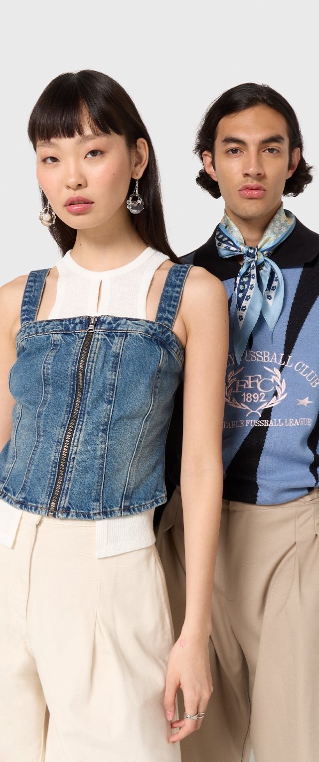 Denim-Crop-Top mit dünnen Trägern und Reißverschluss vorne, kombiniert mit beigen hochgeschnittenen Hosen. Mann in einem gestreiften Hemd mit einem Schal.