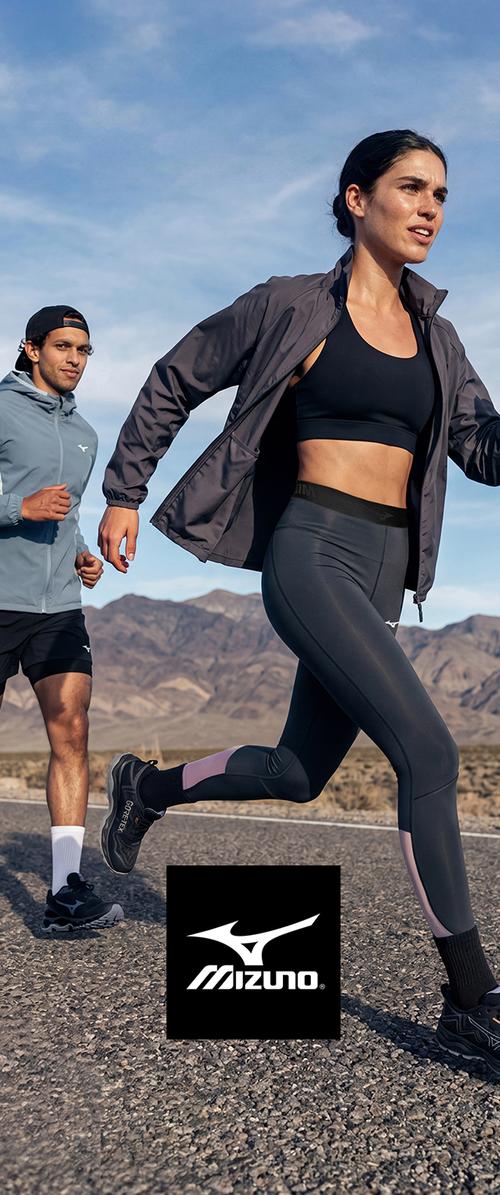 Ein Mann und eine Frau laufen im Freien auf einer Bergstraße, tragen Sportbekleidung und Mizuno Laufschuhe unter einem blauen Himmel.