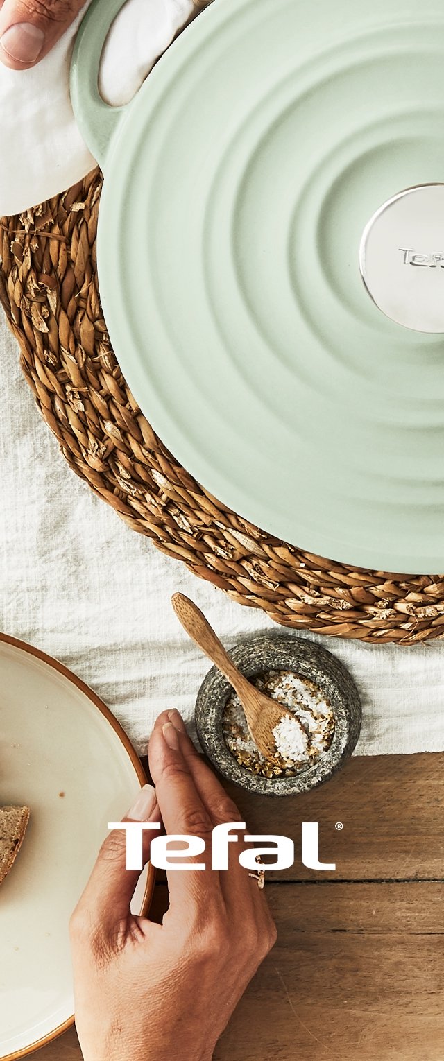 Tefal Keramiktopf in hellgrün mit einem kreisförmigen Design, auf einem gewebten Platzset, neben einer Schale mit Salz und Brot.