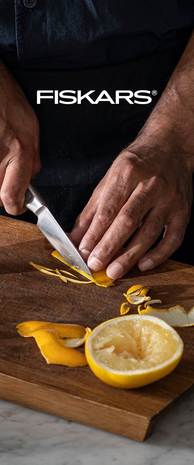 Fiskars-Messer schneidet Zitronenschale auf einem Holzschneidebrett; die leuchtend gelbe Zitrone ist halbiert und zeigt ihr saftiges Inneres.
