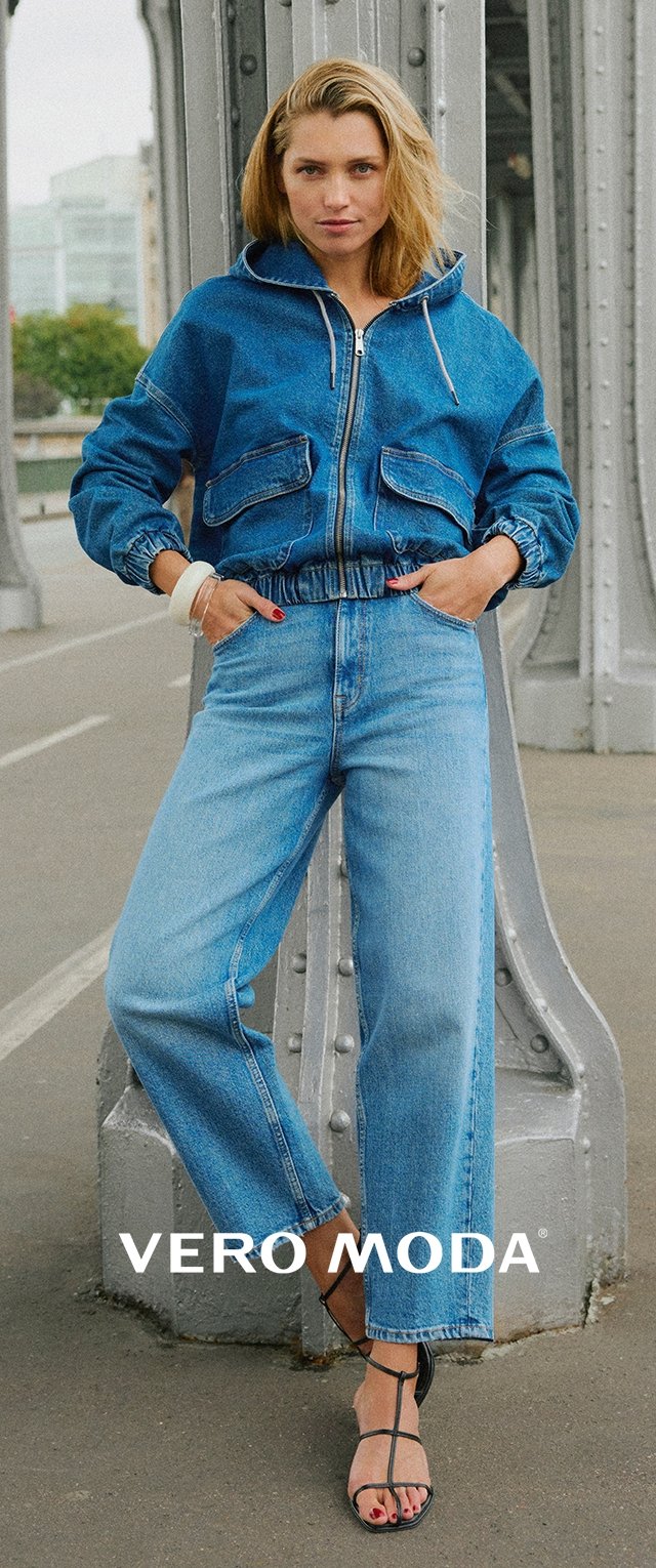 Jeansjacke mit Kapuze und frontalen Taschen, kombiniert mit hochtaillierten, weiten Jeans in einem hellblauen Waschlook. Schwarze Riemchensandalen.