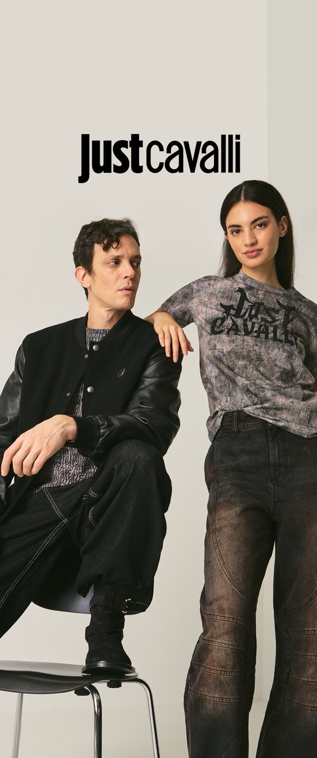 Veste bomber noire avec manches en cuir, t-shirt gris texturé avec logo, pantalon en denim foncé, mannequin posant sur une chaise devant un fond neutre.