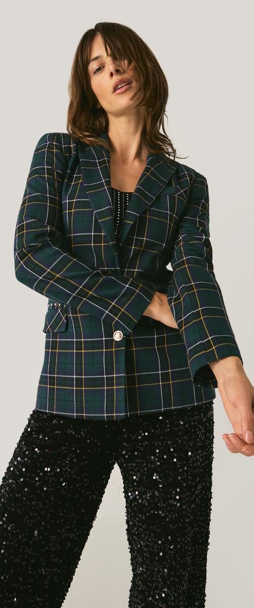 Blazer de cuadros verdes con líneas en azul marino, blanco y amarillo, con dos botones y corte entallado. Combinado con pantalones negros con lentejuelas.