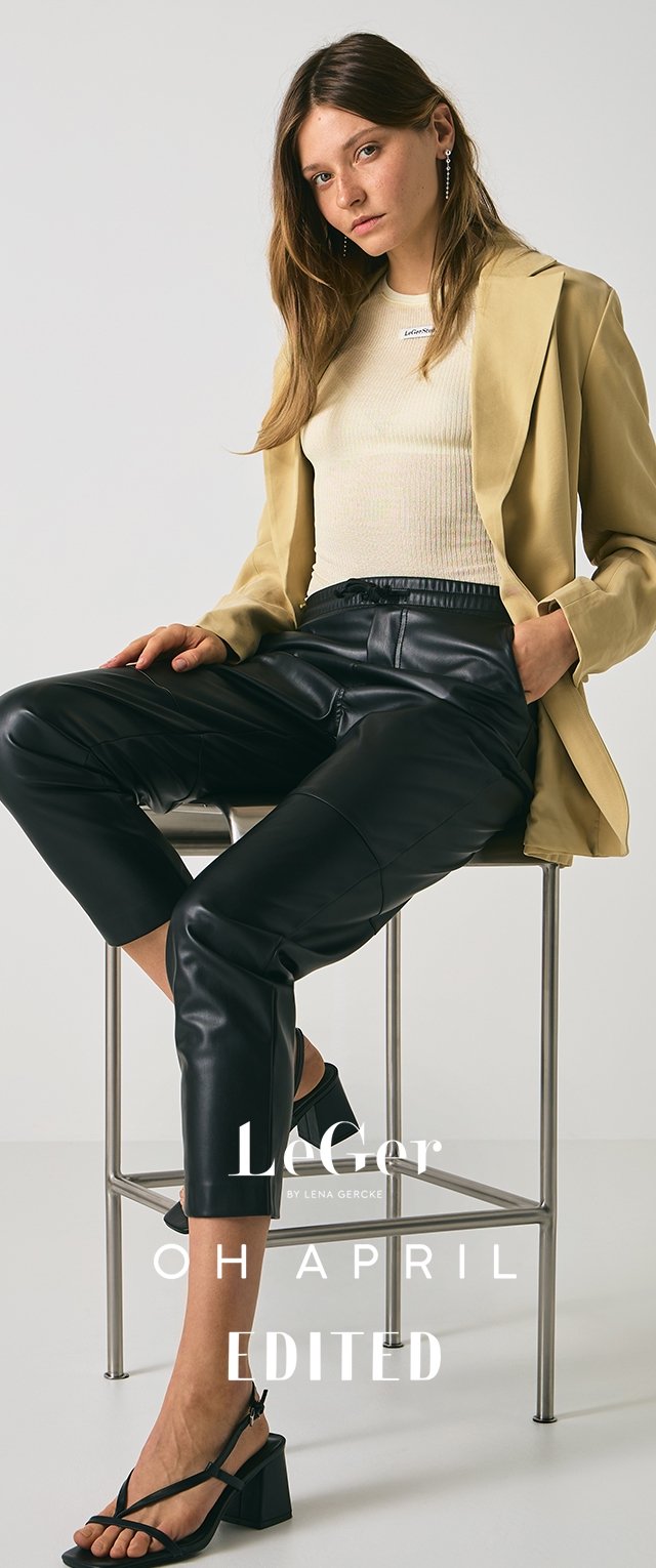 Blazer beige sobre una blusa ligera de canalé, combinado con pantalones de cuero negros ajustados y sandalias de tacón cuadrado negras. Diseño minimalista y textura elegante.