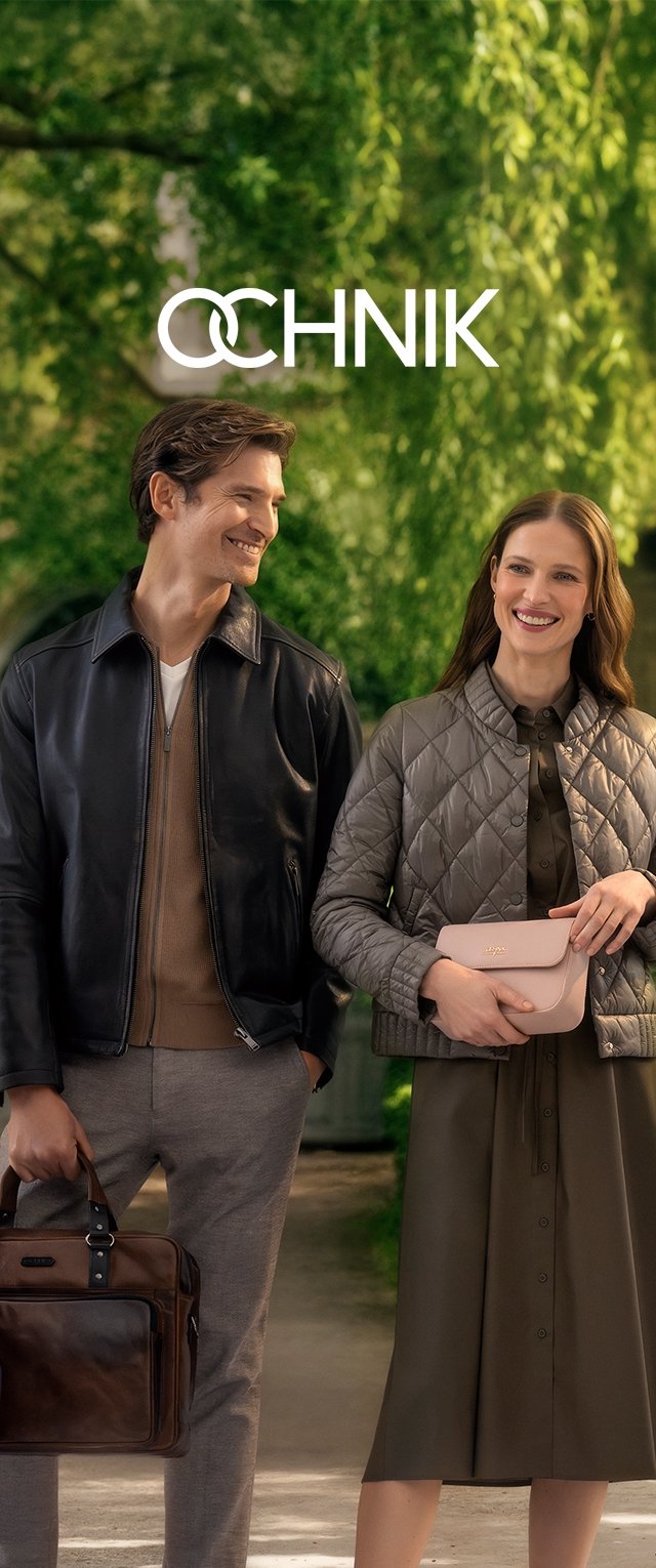 Un homme portant une veste en cuir noire et un sac à main marron ; une femme dans une veste taupe matelassée tient un sac rose ; tous deux portent des vêtements de couleurs neutres.