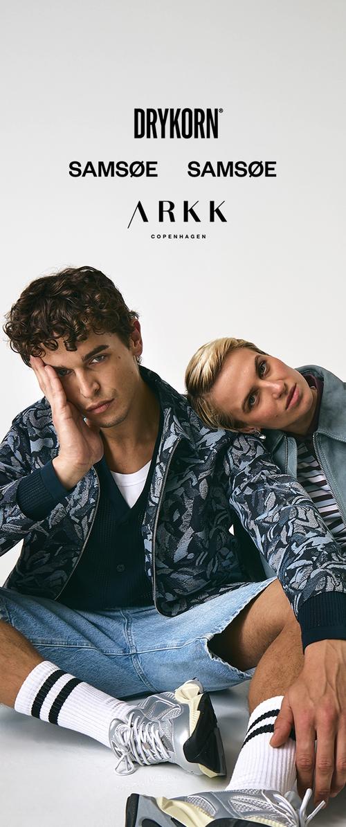 Deux modèles sont assis côte à côte, portant une veste bomber à motifs, un bomber bleu clair et un t-shirt graphique. Ils sont associés à des baskets sportives et des chaussettes blanches.