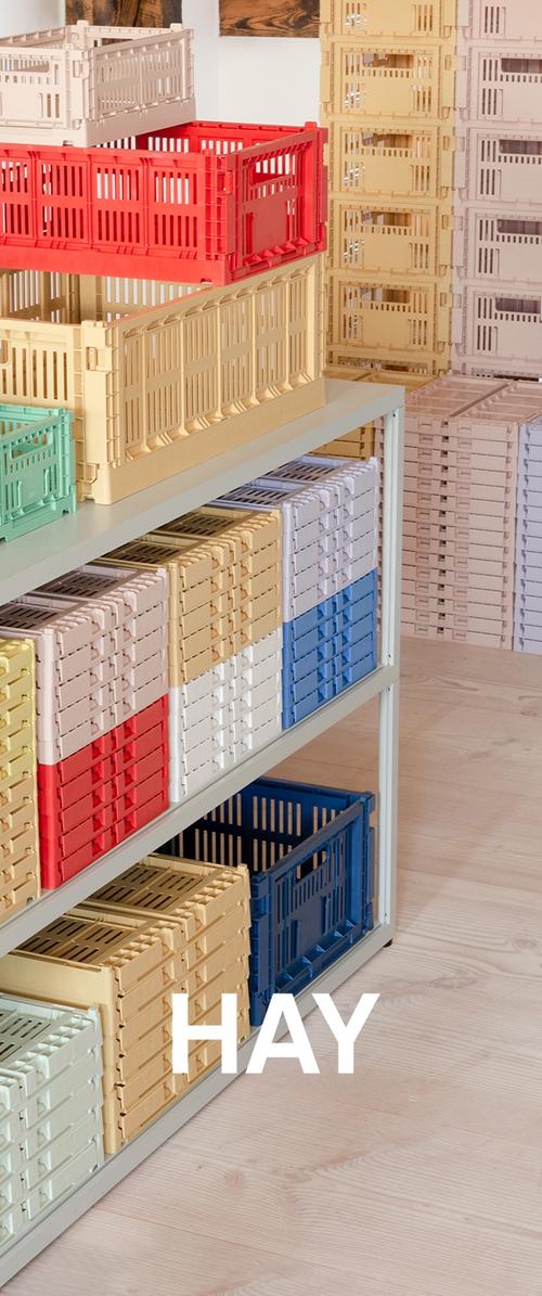 Des caisses en plastique empilées de différentes couleurs (rouge, bleu, vert, beige) organisées sur une étagère en métal, présentant un design perforé.