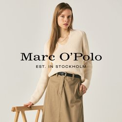 Žena v krémovém svetru, béžové midi sukni, černém pásku a černých mokasínách stojí vedle dřevěného skládacího stojanu na jednobarevném pozadí.