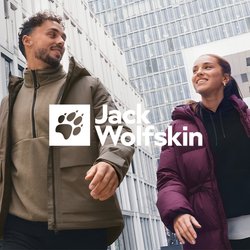 Dva lidé v zimních bundách kráčejí a usmívají se před moderními kancelářskými budovami v městském prostředí za zataženého dne.